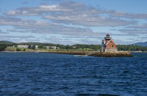 The Rockland Lighthouse sits to the right of the image with the shore in the background and the ocean all around.